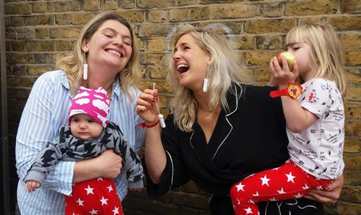 two moms laughing while holding their kids